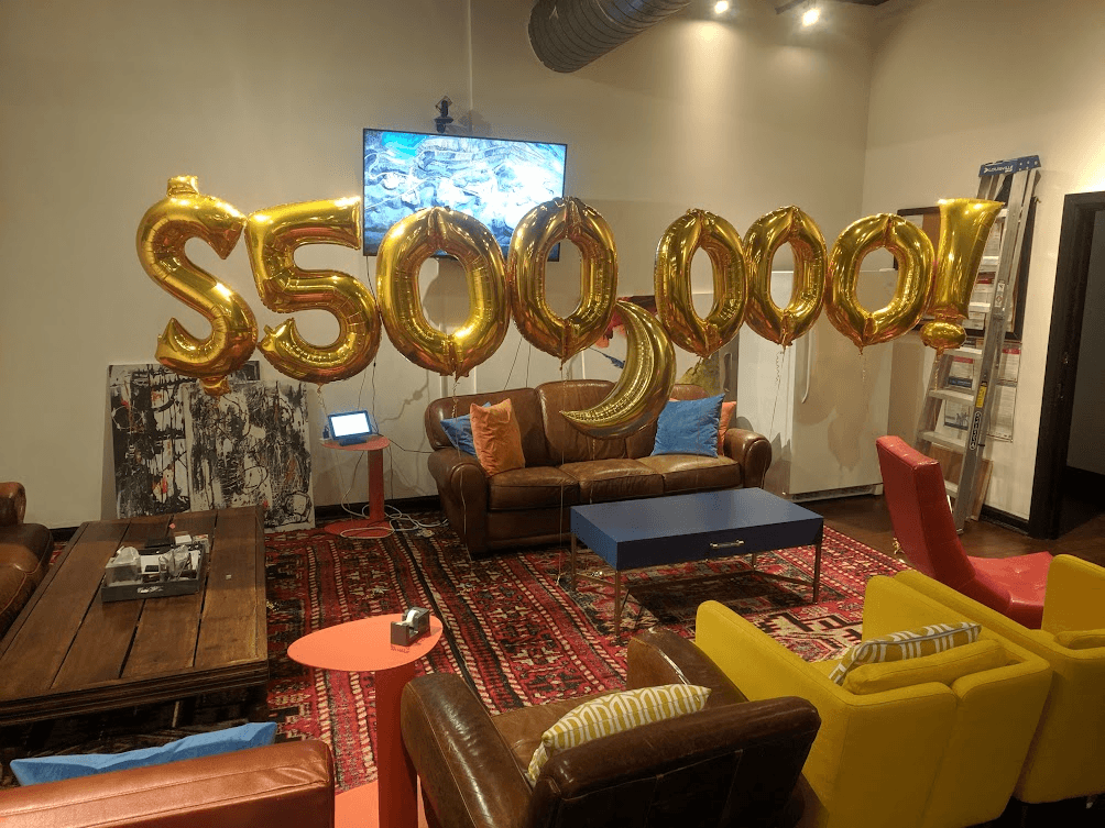 Gold balloons spelling $500,000! floating above the Codecademy office lounge — celebrating the first half-million-dollar revenue month